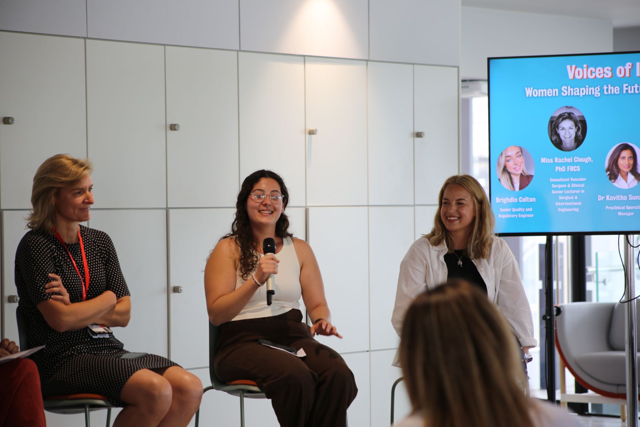 Adriana speaking into a microphone on a Women in STEM panel alongside fellow panellists